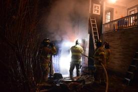 Saranac Lake volunteer firefighters spray down some flames that briefly sprung up as they work on containing an outdoor sauna fire in a backyard on Sunday night. (Enterprise photo — Aaron Marbone)
