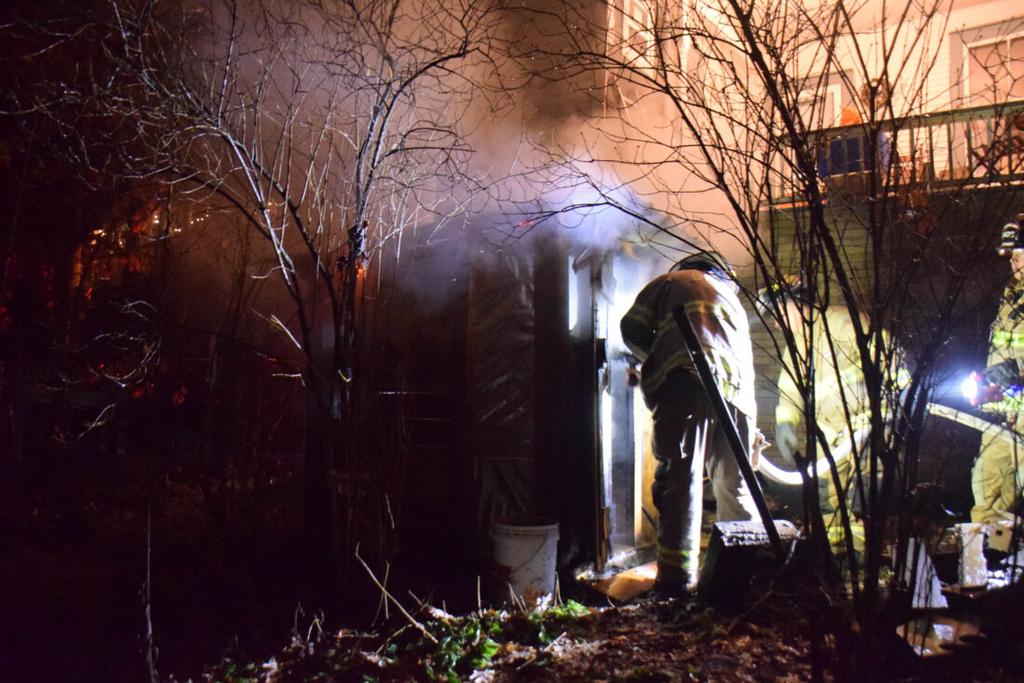 Saranac Lake volunteer firefighters spray down some flames that briefly sprung up as they work on containing an outdoor sauna fire in a backyard on Sunday night. (Enterprise photo — Aaron Marbone)