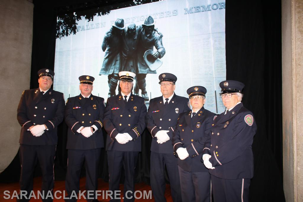 SLVFD Members pose on stage with memorial on screen behind them